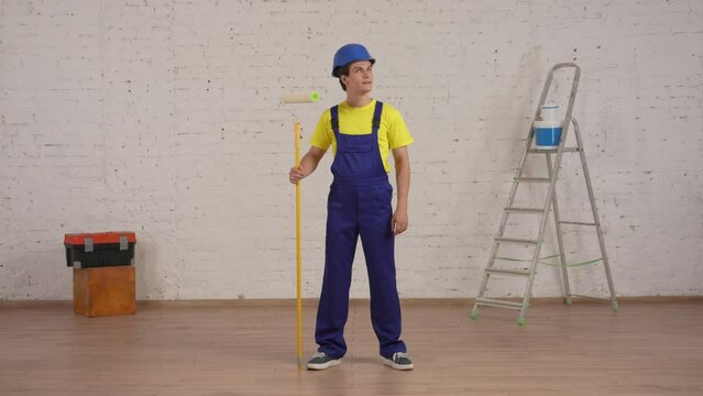 Full length video of a smiling young worker standing in the room with a roller, looking at freshly painted walls and showing OK sign.