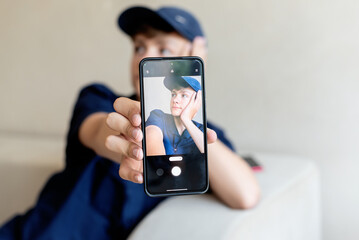 teenage boy holding a smart phone in front of his face at home, taking selfies with his smartphone, digital display on foreground, teen with his own portrait in smartphone, teen blogging