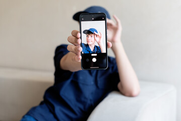teenage boy holding a smart phone in front of his face at home, taking selfies with his smartphone, digital display on foreground, teen with his own portrait in smartphone, teen blogging