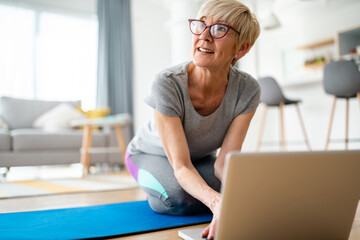 Elderly senior woman in comfortable sports clothes with glasses looking away while surfing the net on laptop.