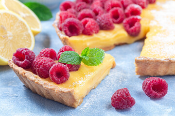 Piece of lemon tart, garnished with fresh raspberry, icing sugar, mint, horizontal, closeup