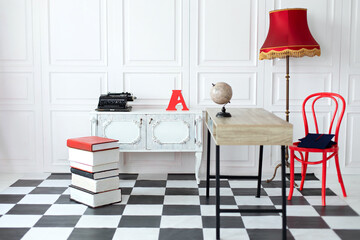 Interior of child room with desktop, red chair and dresser. Modern interior arranged in white and red on chessboard floor and large lamp. Stylish workspace. White minimalist studio