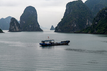 Panoramic view over water of Halong Bay, Vietnam with characteristic monolithic limestone karsts and isles and dense jungle vegetation and fishing boat; UNESCO world heritage site