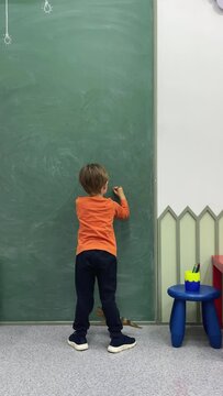 Adorable toddler little boy drawing, writing on blackboard or chalkboard at kindergarten
