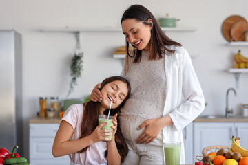 Little girl with her pregnant mother drinking green smoothie in kitchen