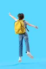 Jumping little boy with schoolbag on blue background, back view