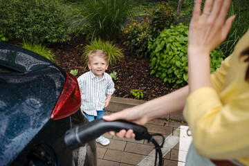 Cute little boy looking at his mother, while she charging electric car.