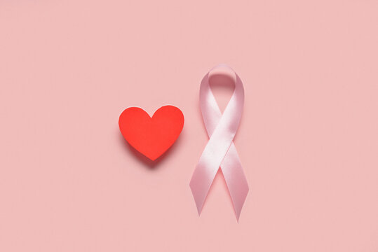 Pink awareness ribbon and red heart on color background. Breast cancer concept