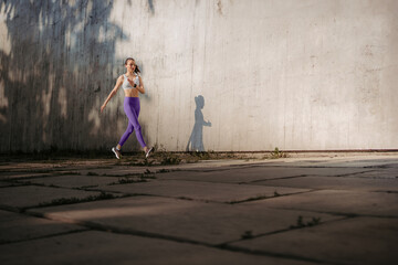 Obraz na płótnie Canvas Fitness woman running in front of concrete wall casting shadow.