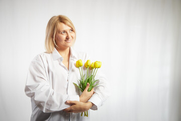 Beauty young blonde happy woman with bouquet of yellow tulips on white background. The concept of a holiday and a gift for a lady and a girl. . Copy space