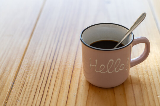 Cup of hot coffee on a wooden table outside the house with a message with the word Hello. Image with copy space.