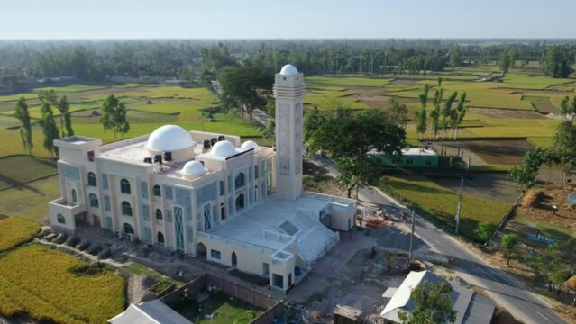 Shot from a drone of Bangladesh's stunning holy model mosque in the midst of rice fields and forests, near to a road.
