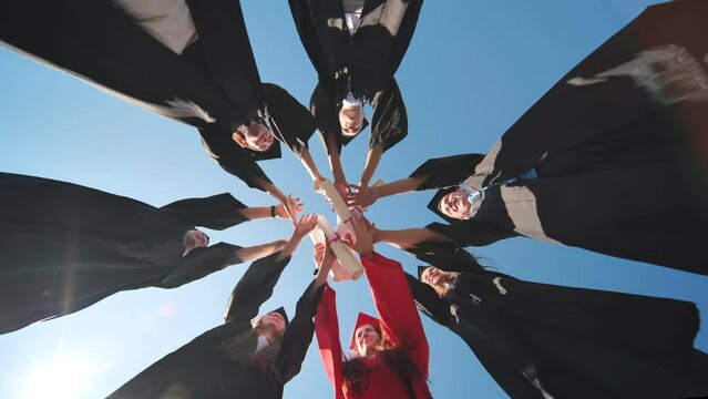 College graduates join hands with diplomas standing in a circle.