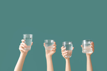 Female hands with glasses of cold water on green background