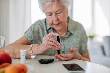 Close up of diabetic senior patient checking her blood sugar level with fingerstick testing glucose meter. - obrazy, fototapety, plakaty
