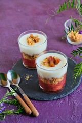 Portioned dessert in a glass with rhubarb jam, shortbread crumble and custard on a purple concrete background. Rhubarb recipes. British cuisine.