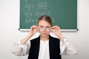 Young math teacher with eyeglasses sitting at wooden table in classroom