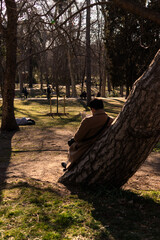 man with his back leaning against a tree reading a book in the park, Retiro Park, Madrid