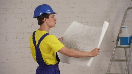 Medium video of a confused young construction worker looking at the plan of the building. Man seems unsure.