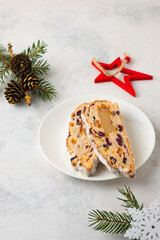 Christmas sweets, slices of stollen with marzipan and dried fruits on a white plate on a light concrete background in Christmas style. Merry Christmas concept