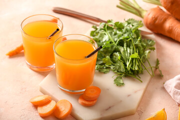 Board with glasses of fresh carrot juice and parsley on pink background