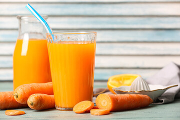 Glass and bottle of fresh carrot juice with orange on blue wooden table