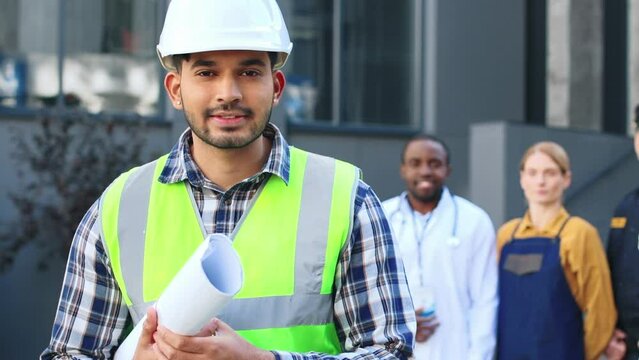 Portrait of architect posing with people of different occupations standing at the background. Jobs concept and diverse professions people. Multicultural team of workers standing outside.