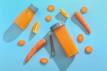 Sports bottles of fresh carrot juice with orange on blue background