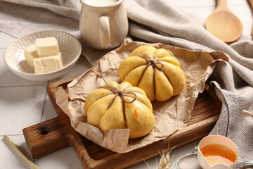 Wooden board with pumpkin shaped buns on white tile background
