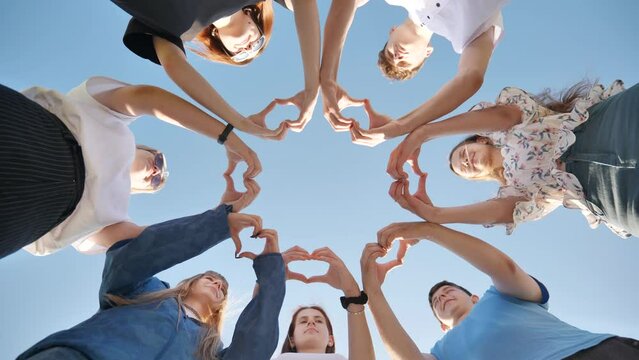 Group of seven people together doing an heart with their fingers and hands - people in cricle having fun and playing - ground view.