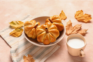 Bowl with tasty pumpkin shaped buns and cup of milk on beige background
