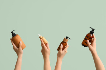 Women with bottles of cosmetic products on green background