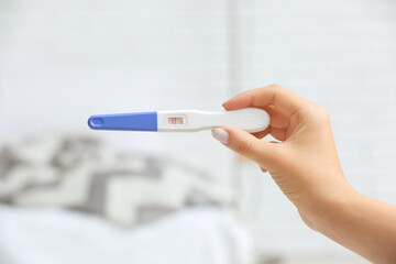 Female hand with positive pregnancy test on light background, closeup