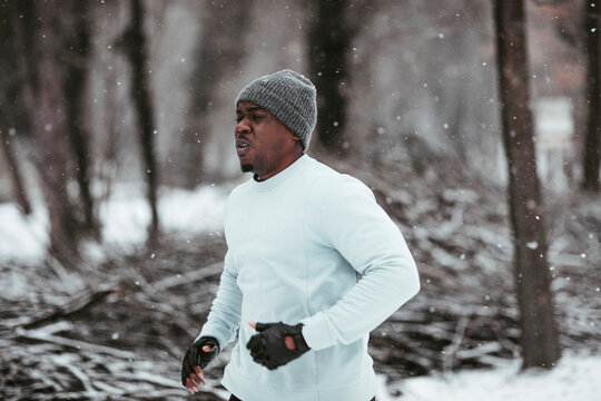 Young african man jogging and running on a forest trail during winter and snow