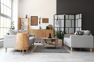 Interior of light living room with grey sofas and coffee table near big window