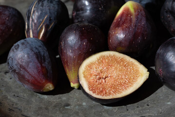 Dark fresh figs lie on an old metal plate. A fig is cut open