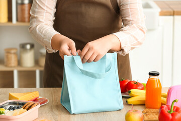 Mother packing meal for school lunch on table in kitchen