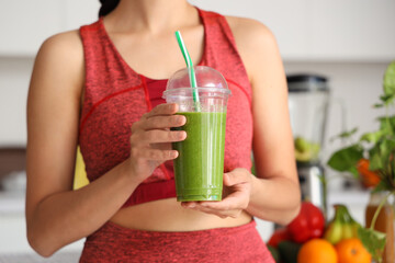 Sporty young woman with healthy smoothie in kitchen, closeup