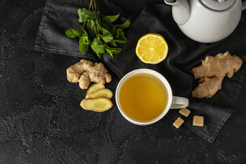 Cup of ginger tea with lemon and mint on black background
