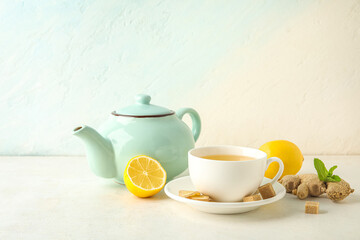 Fototapeta na wymiar Cup of ginger tea with lemon and teapot on white background