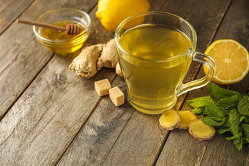 Glass cup of ginger tea and bowl with honey on wooden background