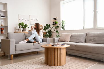 Young woman with book drinking coffee on couch in living room