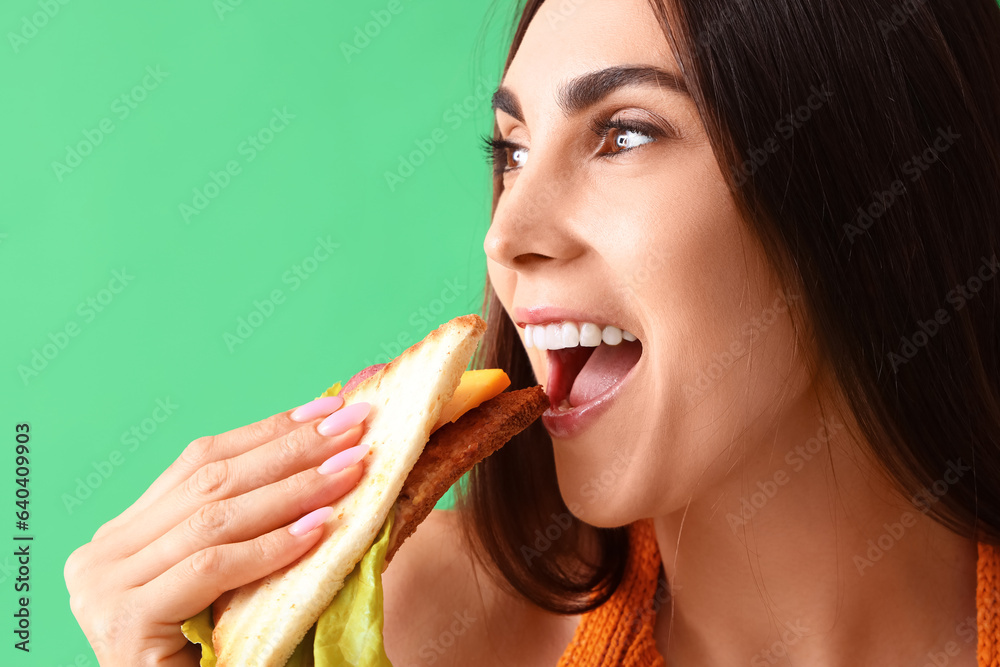 Wall mural Young woman eating tasty sandwich on green background, closeup