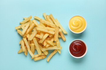 Golden french fries with ketchup and cheese sauce on blue background