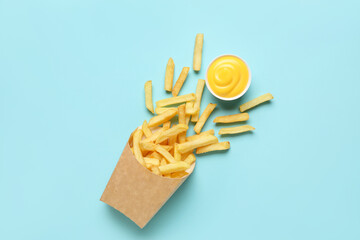 Paper bag with golden french fries and cheese sauce on blue background
