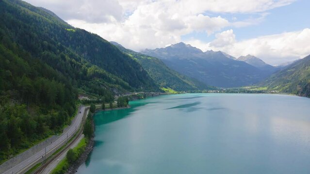 Aerial drone view of Poschiavo alpine lake and road in the Switzerland mountains. Miralago Bernina Express train station. Swiss Alps