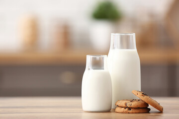 Bottles of fresh milk with sweet cookies on wooden table in kitchen