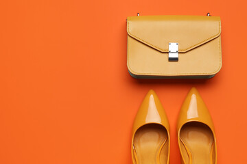Stylish yellow high heels and purse on orange background