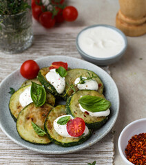 Zucchini fried on a plate with basil and cherry tomatoes, sour cream sauce and spices in bowls,...