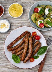 Grilled sausages on a plate with vegetables, herbs, sauce and mustard, top view..
